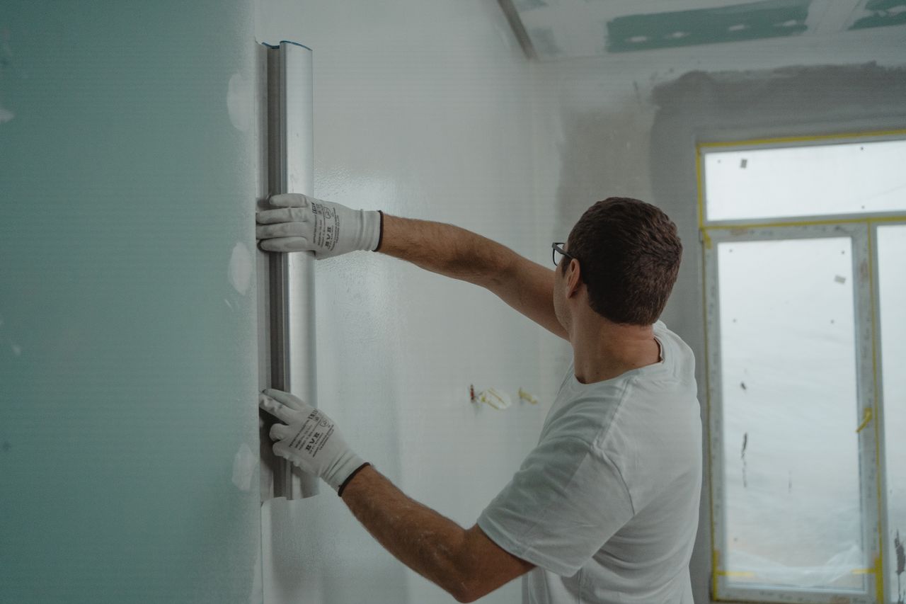 Crafting Captivating Headlines: Your awesome post title goes here A man in a white shirt and gloves using a metal ruler for indoor wall renovation work.